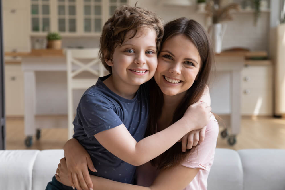 Mother and son sitting on the couch side hugging each other with smiling faces 