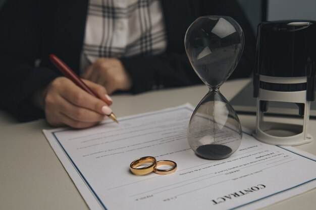 A woman signing a document with a wedding ring and an hourglass, indicating the passing of time.