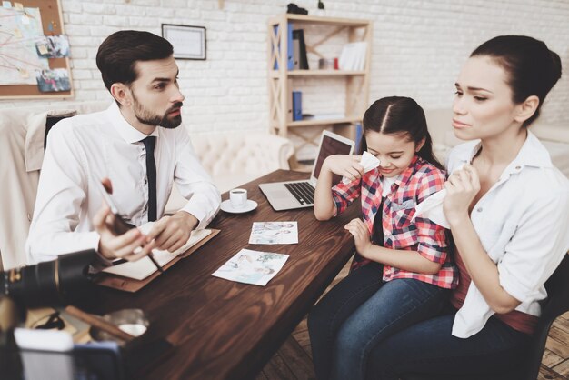 A family at a financial advisor's office with the child distracted by a phone while the parents discuss finances.