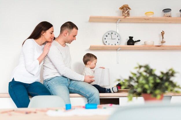 A family spending time together in a kitchen with a child playing and the parents sitting nearby.