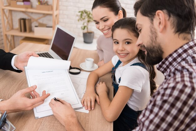 A family is sitting together at a table with a man in a suit who is presenting a document for signature.