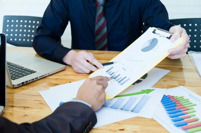 Two businessmen reviewing graphs and data charts with a laptop and additional documents on the table.