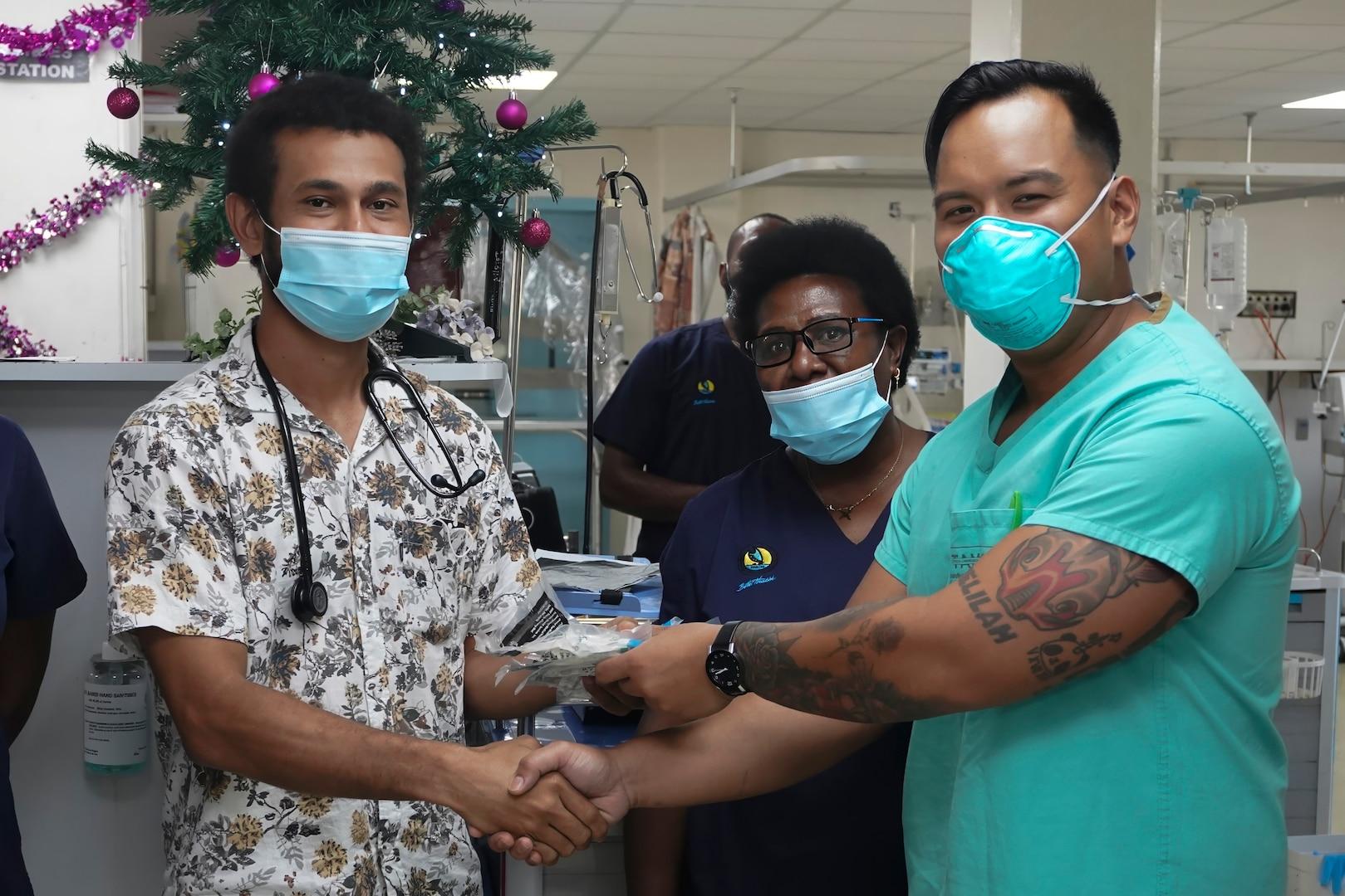 Two healthcare workers, wearing masks and scrubs, shake hands in a hospital setting adorned with Christmas decorations. A woman in scrubs and a mask stands behind them. Nearby, a sign reminds staff about secure health info sharing and the importance of the HIPAA Release Form Texas.