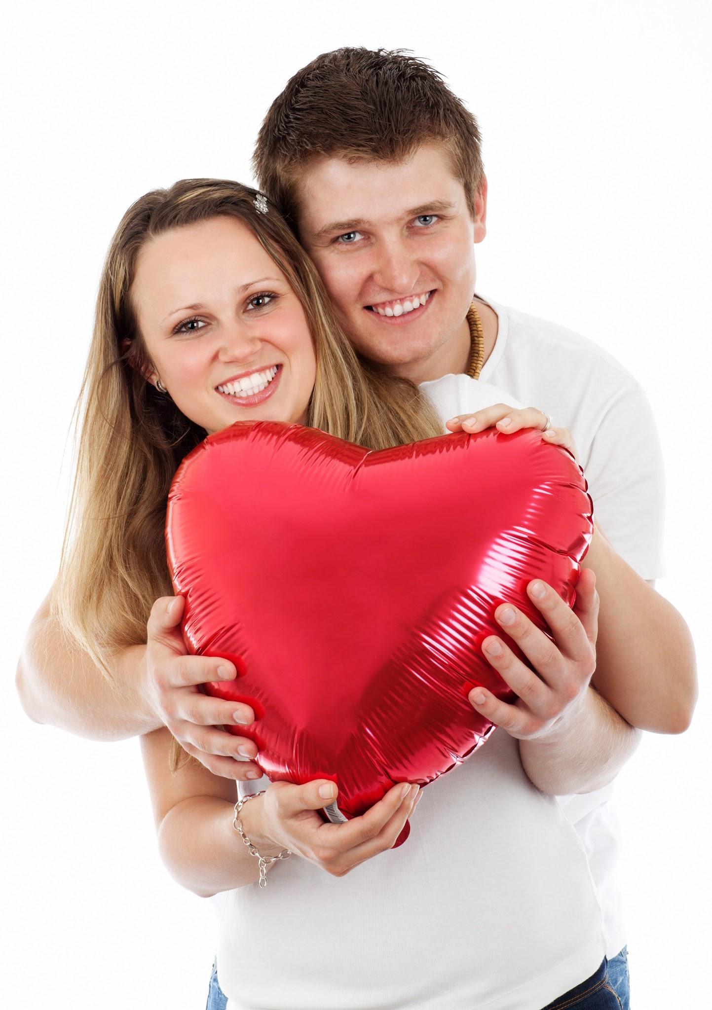 A smiling couple holding a large red heart-shaped balloon together.