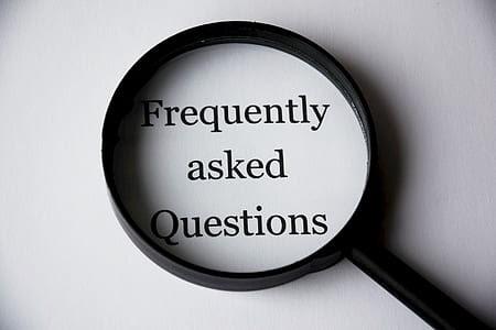 A magnifying glass is placed over the text "Frequently asked Questions" on a white background.