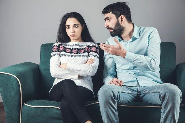 A man speaks to a woman sitting on a green couch with her arms crossed, looking away from him, as they discuss the importance of post-divorce modifications.