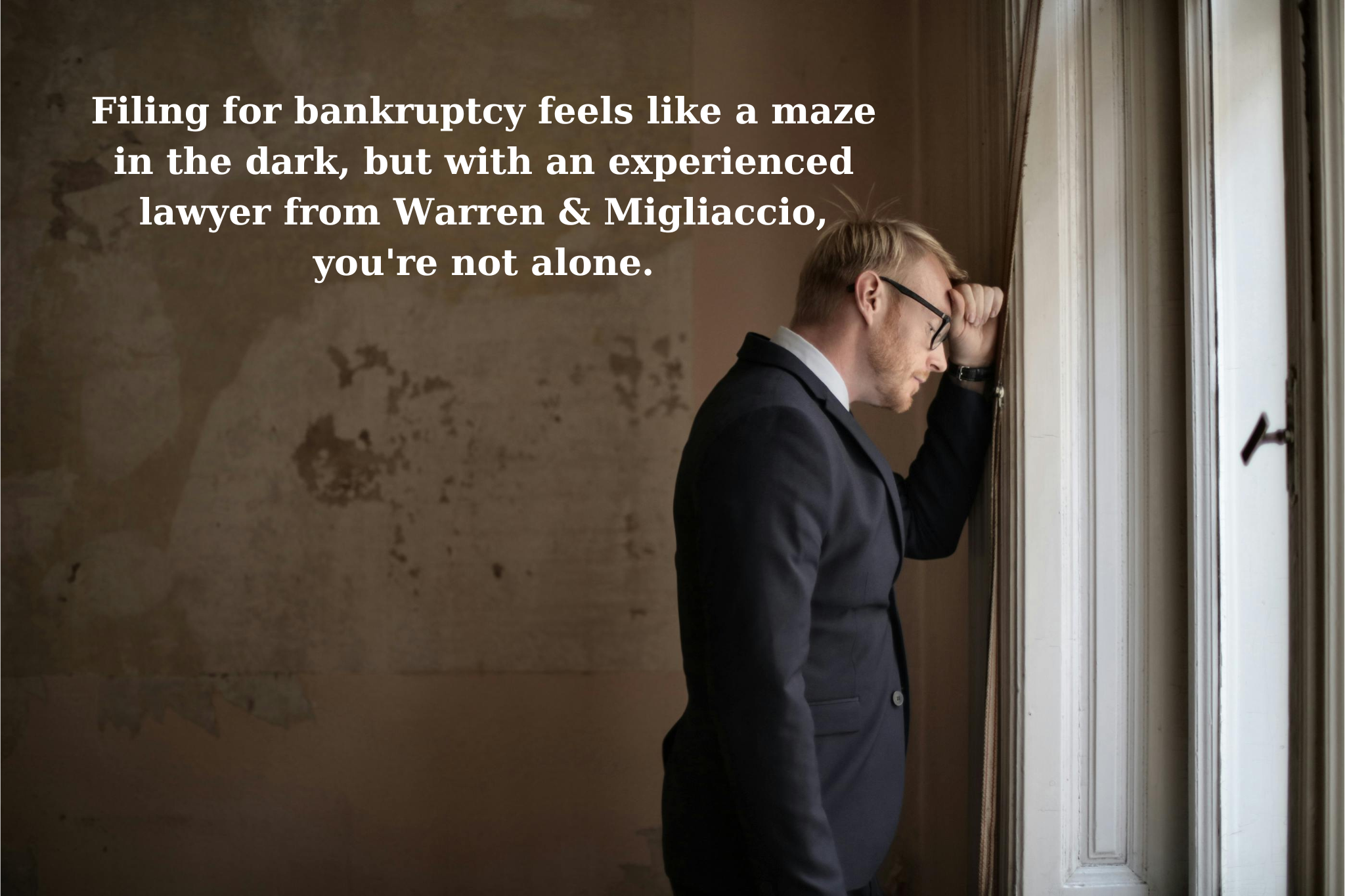 A man in a suit, looking stressed, leans his head against a window. Text overlay reads: "Filing for bankruptcy feels like a maze in the dark, but with an experienced lawyer from Warren & Migliaccio, you're not alone. Do I have to go to court for Chapter 7? Let us guide you through the process.