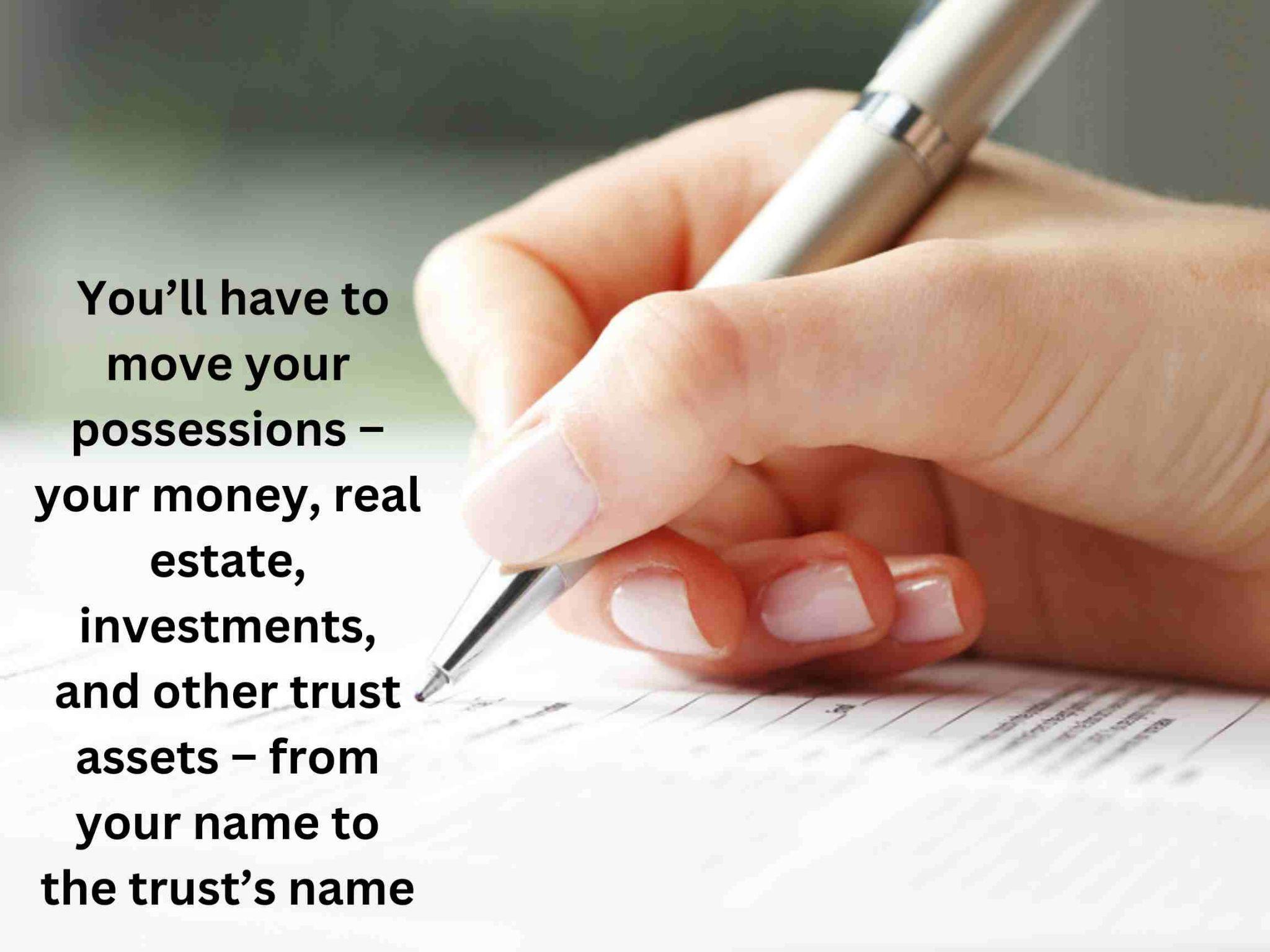 A hand holding a pen writes on paper. Text reads: "You’ll have to move your possessions – your money, real estate, investments, and other trust assets – from your name to the trust’s name. 